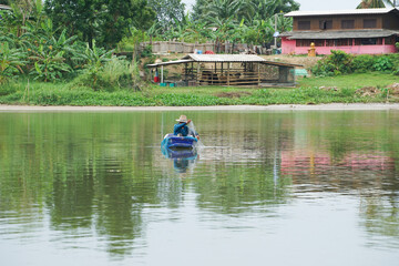 Lonely man sits in the boat and collects the fish from the net with forest in background.