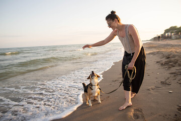 young woman with a beagle dog having fun by the sea