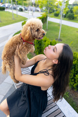 Beautiful Caucasian girl and her pet, little golden poodle dog strolling in public park, outdoors. Summer time. Sincere emotions. leisure activities concept