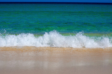 Crystal clear blue sea water in various shades, white foam and  wave flooding the sandy beach. Fuerteventura, Canary islands, Atlantic ocean.