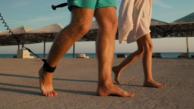 Summer vacations. Father and daughter are walking to surf with a sup board. Sunset light. Feets close up. Slow motion.
