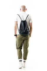 Back view of hipster nerdy style bald shaven man walking with hands in pockets. Full length...