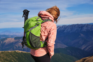 Hiker girl with green backpack and hiking poles in the Carpathian mountains.