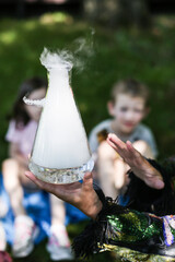 Close up of Chemical Show Animator  hand at birthday party showing fun chemical reaction experiment to group of children (kids). Mixing chemicals in bottle so that they fume. 