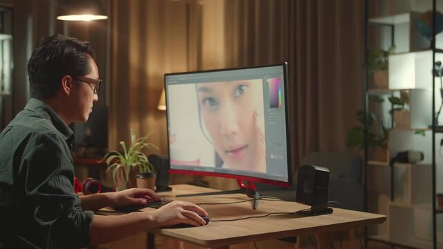 Asian Male Digital Editor Works In Photo Editing Software On His Personal Computer With Big Display, He Works At Night 
