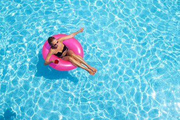 A beautiful young woman on an inflatable circle in blue water. Relaxing in the pool with a cocktail...