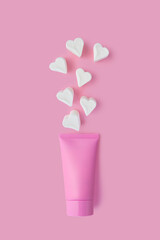 Creative beauty fashion concept photo of cosmetic recyclable bottle lotion cream with marshmallow candy on pink background.