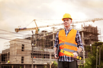 Handsome young man engineer holding laptop and construction level ruler with construction building background.