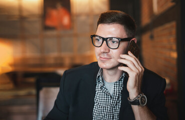 Portrait of young caucasian businessman using smartphone at cafe.