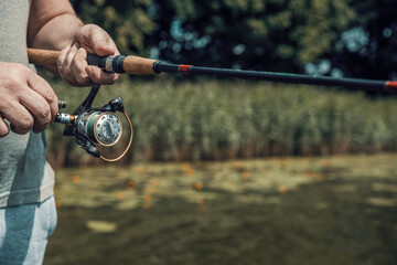 Fishing rod with a spinning reel in the hands of a fisherman in summer. Fishing background.