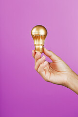 Gold light bulb in a female hand on a pink background, as a concept of ideas and help