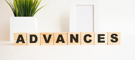Wooden cubes with letters on a white table. The word is ADVANCES. White background.