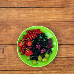 Berry mix - currants, gooseberries, mulberries, strawberries in a plate on a wooden background with copy space. Summer concept.