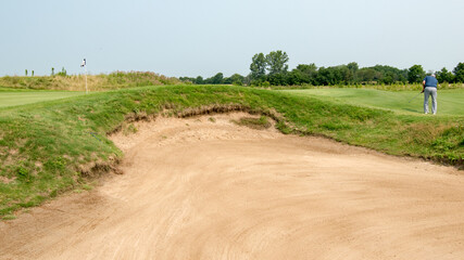 Golfer attempts a long putt behind a bunker on a links course.