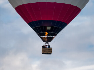 Hot air balloon with basket flies in the sky, visible flame