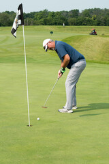 A golfer putting watches his putt approach the hole.