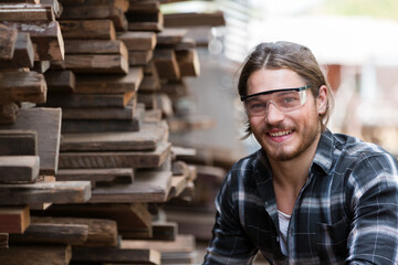 Portrait of male carpenter wearing safety goggles at work. Woodworker examining wood at woodwork workshop