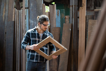 Male carpenter examining piece of wood in carpentry workshop. Carpenter working his job at the workshop