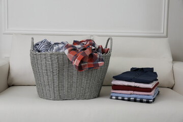 Wicker basket with dirty laundry and stack of clean clothes on sofa indoors