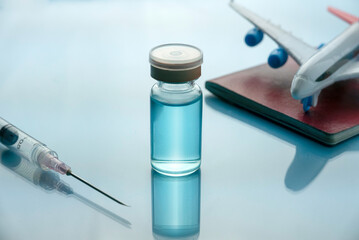 Healthcare,medical, tourism and vaccination concept with vaccine bottle,syringe, passport and plane model on a blue glass background.