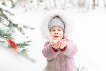 little girl in a warm hat and coat decorates a Christmas tree outdoors. snowy winter
