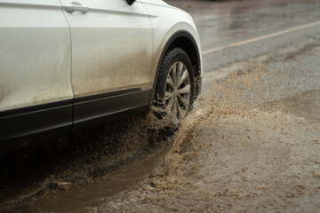 The car is driving in a puddle. White car in the mud.