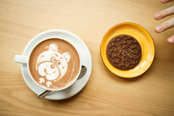 cup of coffee on a wooden table. A child's hand reaches for a chocolate chip cookie and a cup of cocoa with a pattern