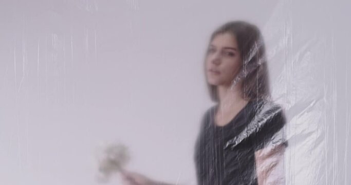 Heartbreak pain. Cheating spouse. Divorce despair. Plant allergy. Defocused sad betrayed woman holding flowers behind transparent plastic film in light out of focus background.