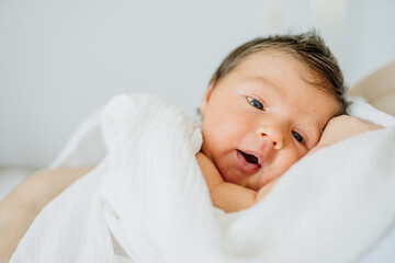 Home portrait of a newborn baby girl in mother's hands on bed. Infant child ten day old in white...