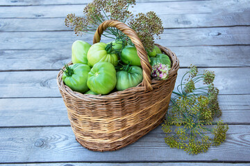 Basket with vegetables and herbs. Tomatoes and dill in a wicker basket on a wooden background.