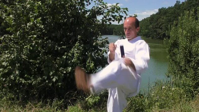 The athlete trains kicks against the background of a pond