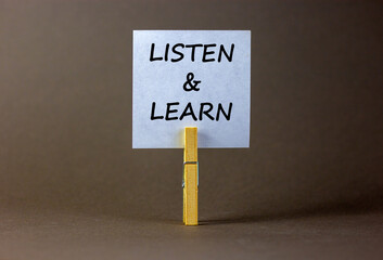 Listen and learn symbol. White paper with words 'Listen and learn', clip on wooden clothespin. Beautiful grey background. Business, educational and listen and learn concept. Copy space.