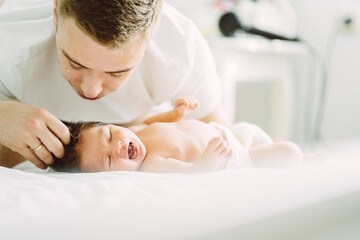 Fototapeta na wymiar Family, fatherhood and people concept. Happy father gently caressing, blowing, kissing and admire newborn little baby daughter at home at sunny light bedroom.