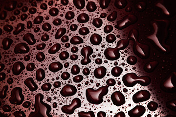 Water droplets on a red surface with light and shadow on the surface.