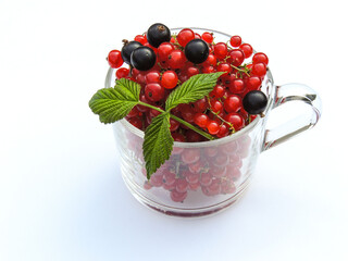 Red and black currants in a transparent cup on a white background