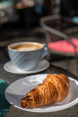 Breakfast with croissant and a cup of cappuccino on the table early sunshine morning in a street cafe.