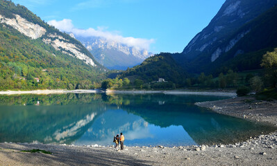 Lago di Tenno with its clear water in the morning light. Two people standing on the bank. Trentino, Italy.