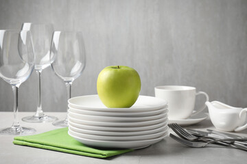 Clean dishware, glasses, cutlery and apple on light grey table