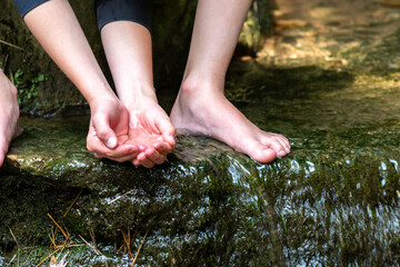 Young boy playing barefoot with clear water at a little creek using his feet and the water spring cooling his toes and legs and refreshing with the pure elixir of life in zen meditation atmosphere