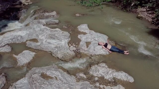 A girl sunbathes in a mountain river on stones, flying over the river