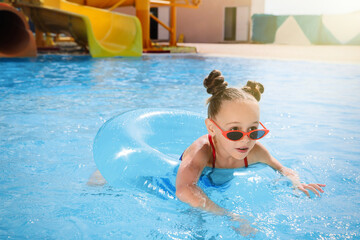 Cute little girl with inflatable ring in swimming pool at water park