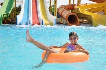 Cute little girl with inflatable ring in swimming pool at water park