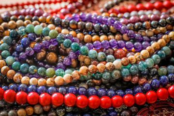 a variety of beads made of natural stones are randomly scattered on the golden surface next to beautiful linen bags of red and beige colors