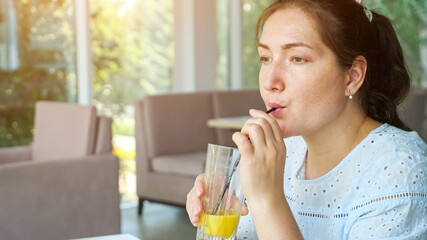 Attractive young lady drinks juice in cafe, side view