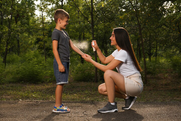 Woman applying insect repellent on her son's arm in park. Tick bites prevention - obrazy, fototapety, plakaty