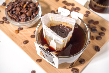 Instant freshly brewed cup of coffee from bag. Trendy variety of drip coffee, on white kitchen table with cups, copy space
