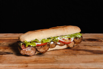 Small meat and vegetable sandwich on a wooden table with a black background