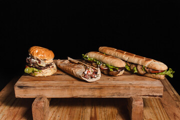A hamburger, Arabian tenderloin and two steak sandwiches on top of a raised wooden table with a...