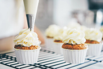 Woman making creamy top of cupcakes closeup. Selective focus.