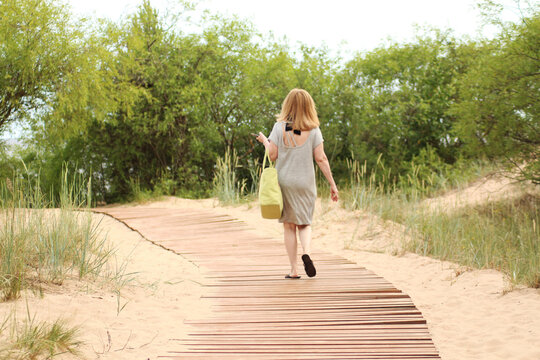 A woman on vacation walks along a wooden bridge to the beach by the sea. The sandy beach has a wooden path to the sea. Female